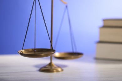 Photo of Scales of justice and books on table against light blue background, closeup