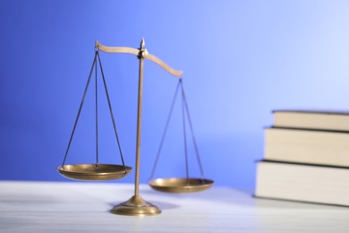 Photo of Scales of justice and books on table against light blue background