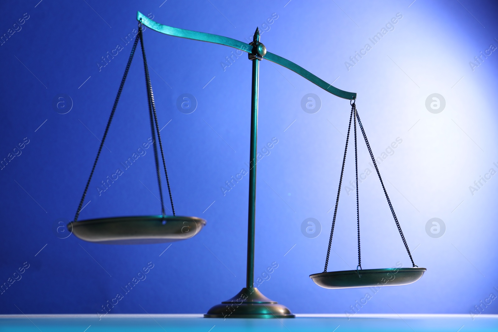 Photo of Scales of justice on table against blue background
