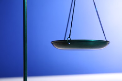 Photo of Scales of justice on table against light blue background, closeup
