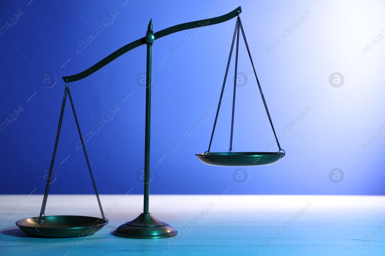 Photo of Scales of justice on table against blue background