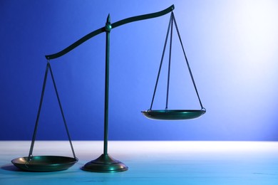 Photo of Scales of justice on table against blue background