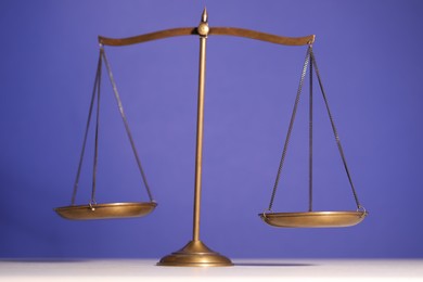 Photo of Scales of justice on table against violet background