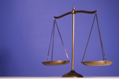 Photo of Scales of justice on table against violet background