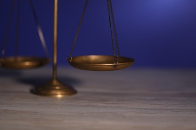 Photo of Scales of justice on wooden table against dark background, closeup