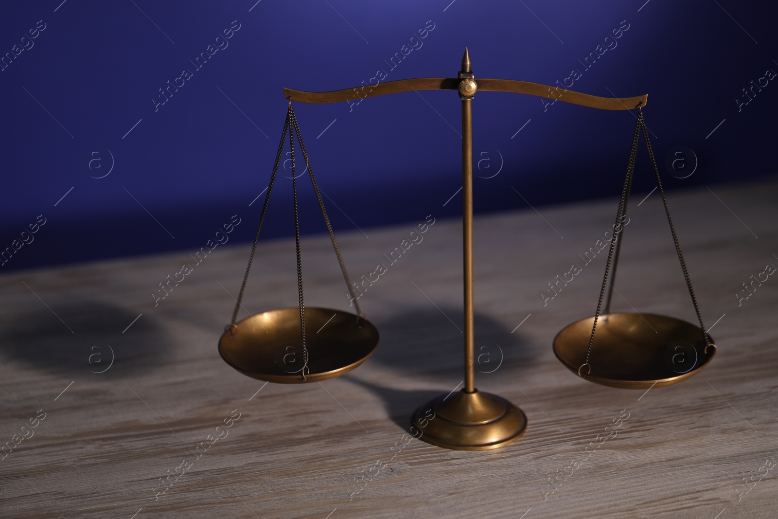 Scales of justice on wooden table against dark background Photo of Scales of justice on wooden table against dark background