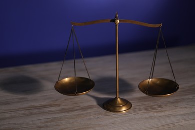 Photo of Scales of justice on wooden table against dark background