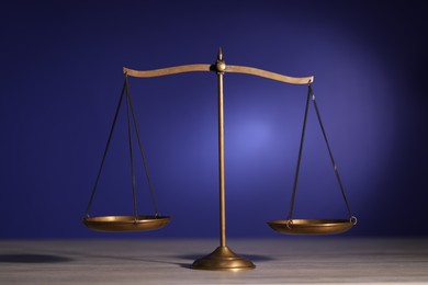 Photo of Scales of justice on wooden table against dark background