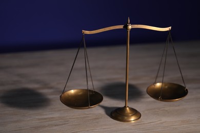 Photo of Scales of justice on wooden table against dark background