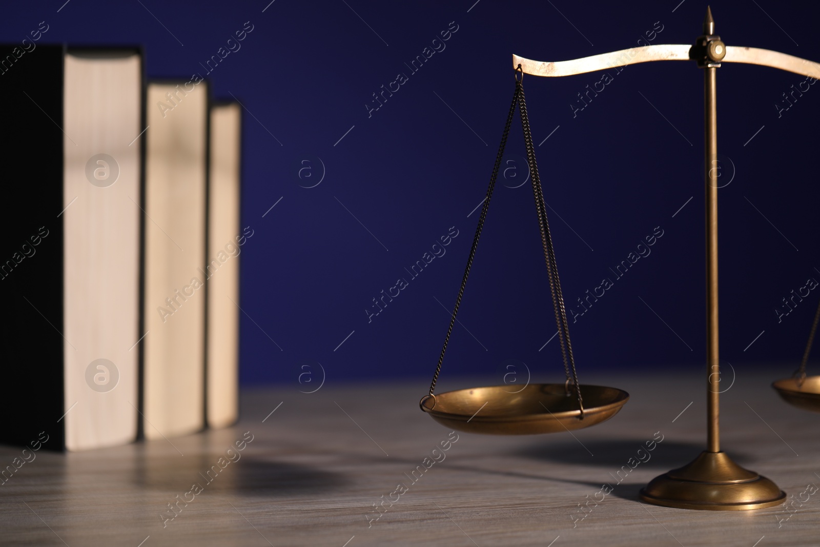 Photo of Scales of justice and books on wooden table against dark background