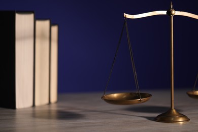 Photo of Scales of justice and books on wooden table against dark background
