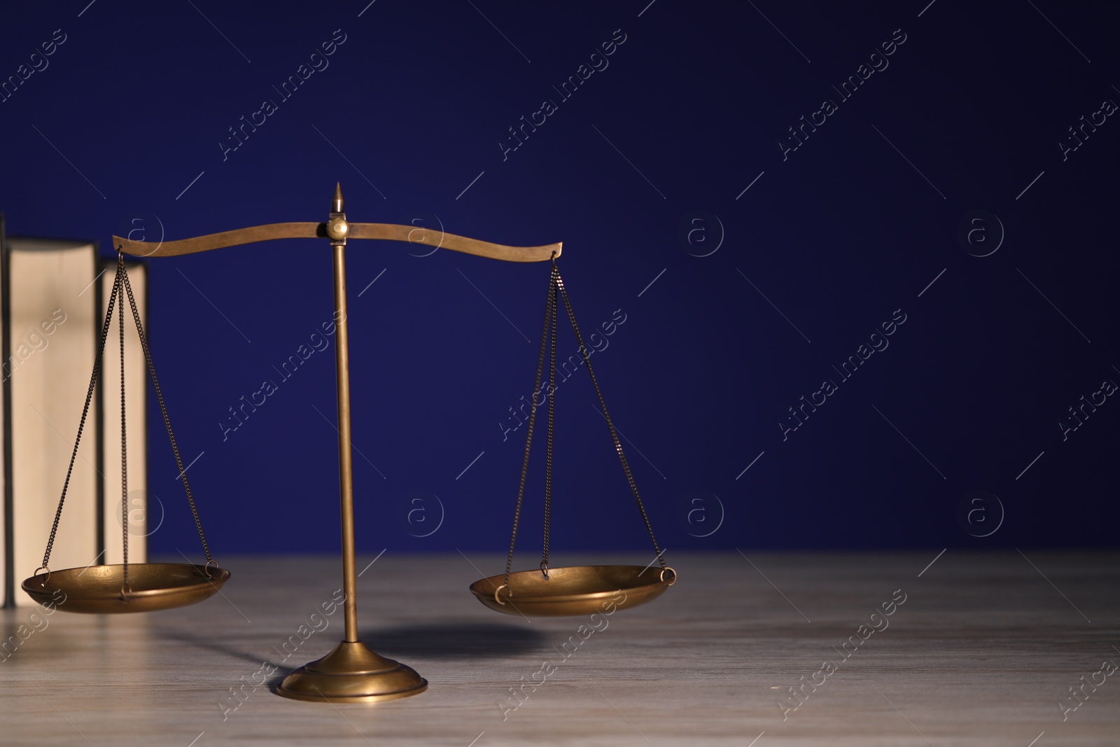 Photo of Scales of justice and books on wooden table against dark background. Space for text