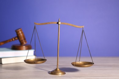 Photo of Scales of justice, books and judge's gavel on wooden table against violet background