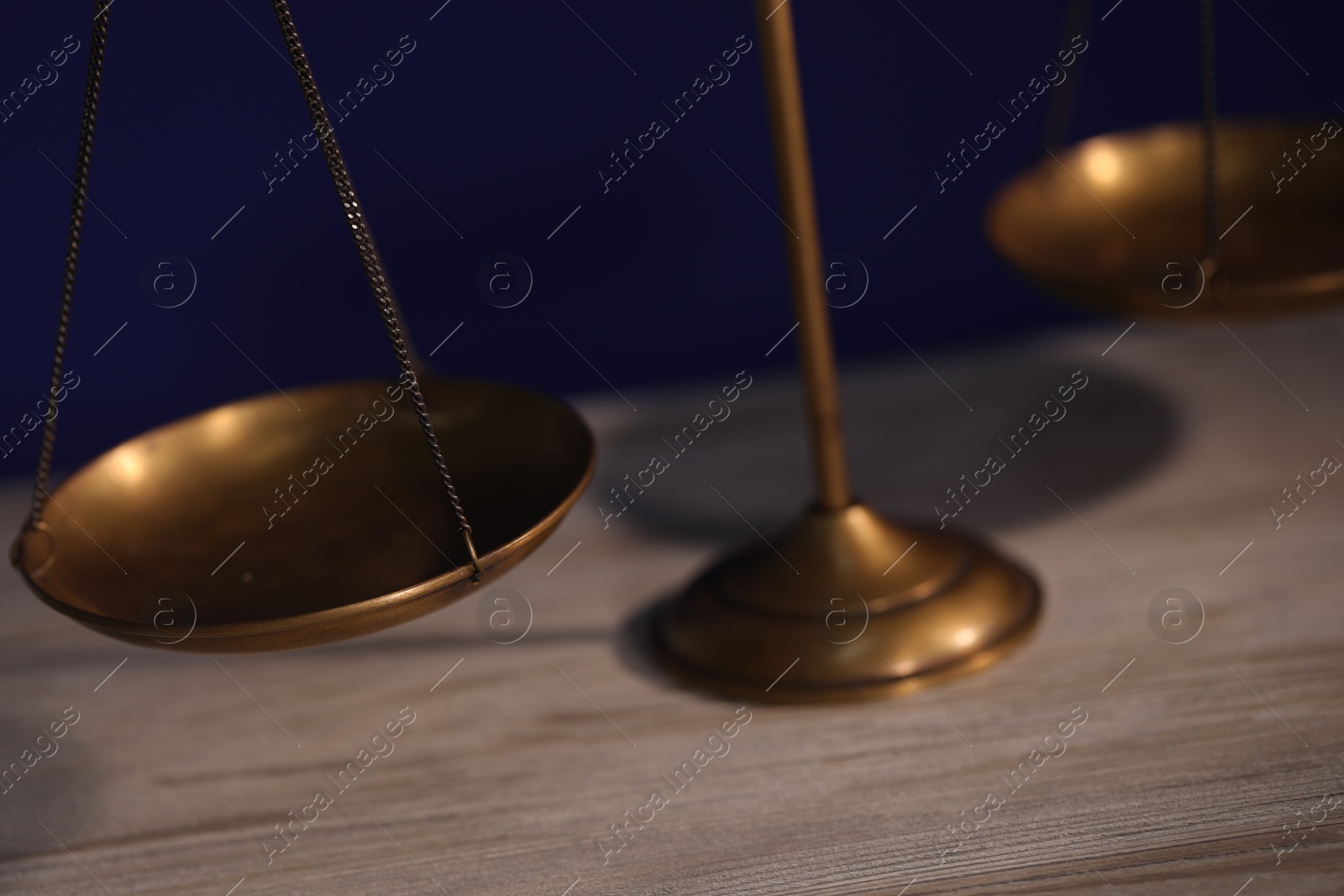 Photo of Scales of justice on wooden table against dark background, closeup