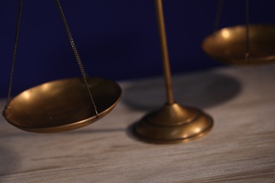 Photo of Scales of justice on wooden table against dark background, closeup