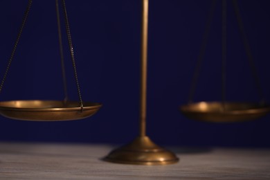Photo of Scales of justice on wooden table against dark background, closeup