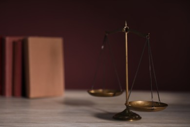 Photo of Scales of justice and books on wooden table against dark background, selective focus