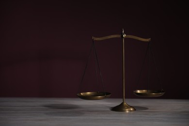 Photo of Scales of justice on wooden table against dark background. Space for text