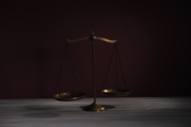 Photo of Scales of justice on wooden table against dark background