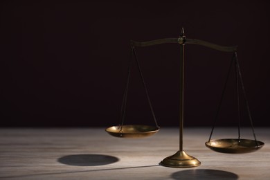 Photo of Scales of justice on wooden table against dark background. Space for text