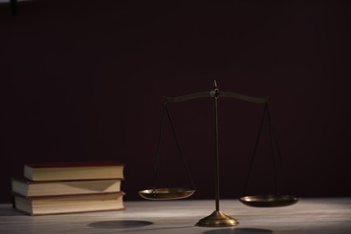 Photo of Scales of justice and books on wooden table against dark background