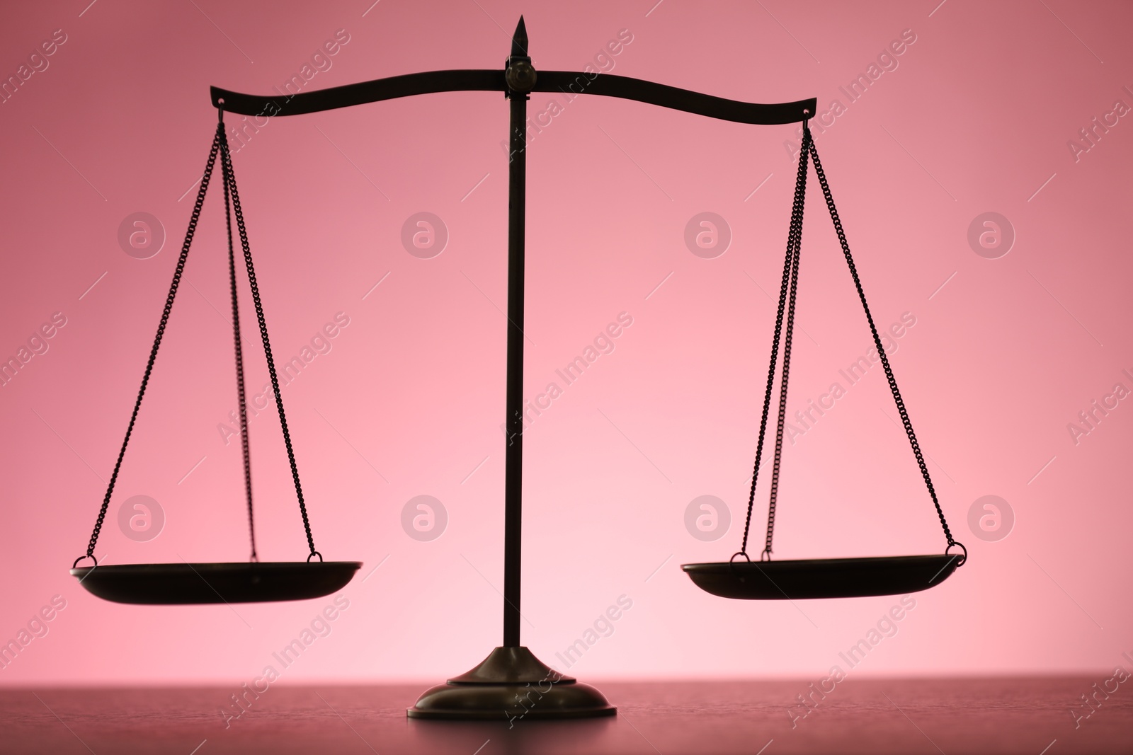 Scales of justice on table against color background Photo of Scales of justice on table against color background