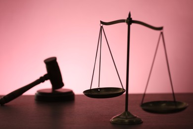 Photo of Scales of justice and judge's gavel on table against color background, selective focus