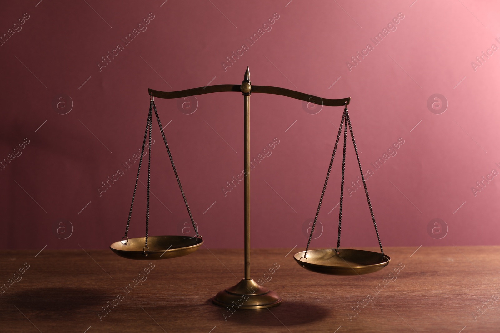 Scales of justice on table against color background Photo of Scales of justice on table against color background