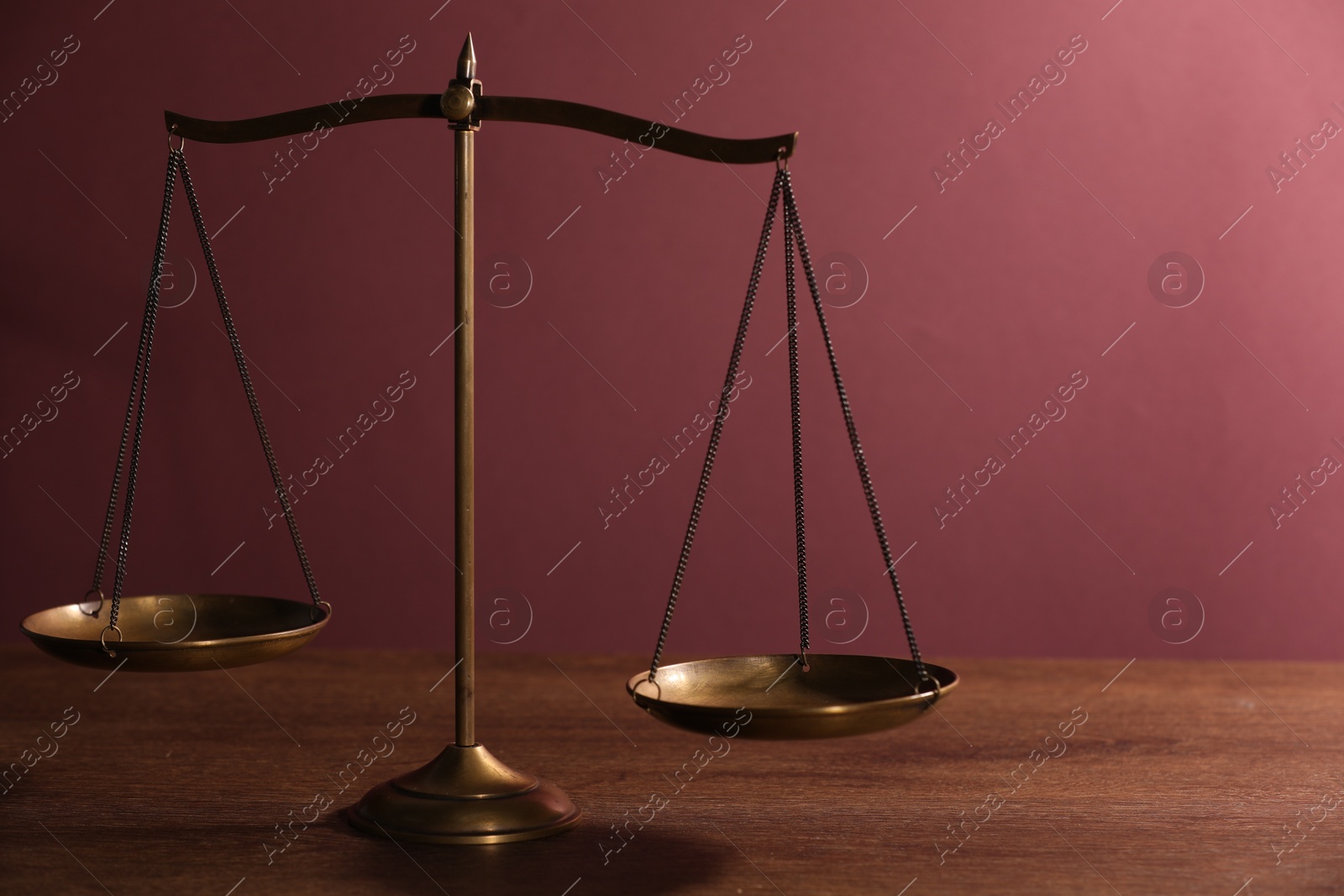 Scales of justice on wooden table against color background Photo of Scales of justice on wooden table against color background