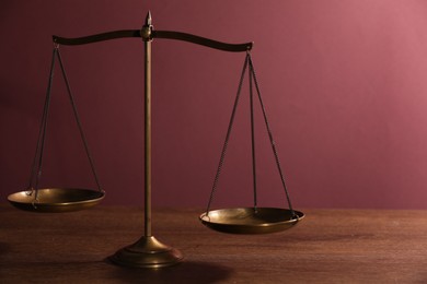 Photo of Scales of justice on wooden table against color background