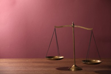 Photo of Scales of justice on wooden table against color background. Space for text