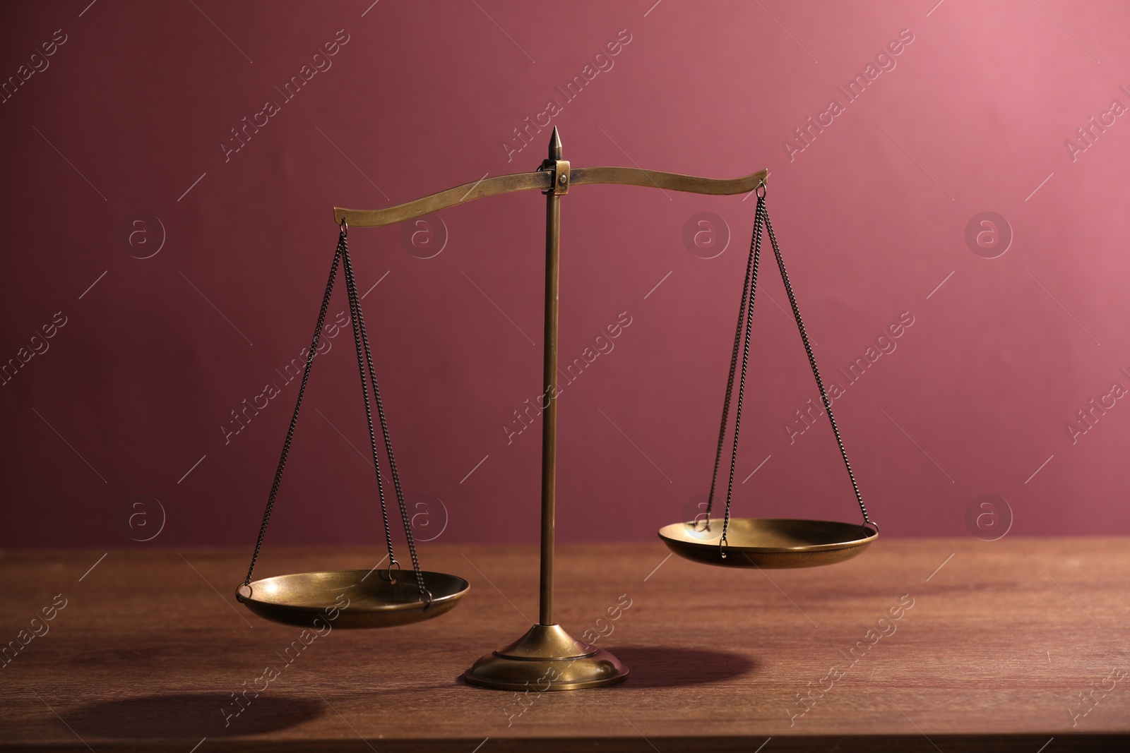Scales of justice on wooden table against color background Photo of Scales of justice on wooden table against color background