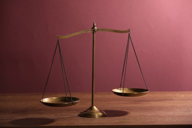 Photo of Scales of justice on wooden table against color background