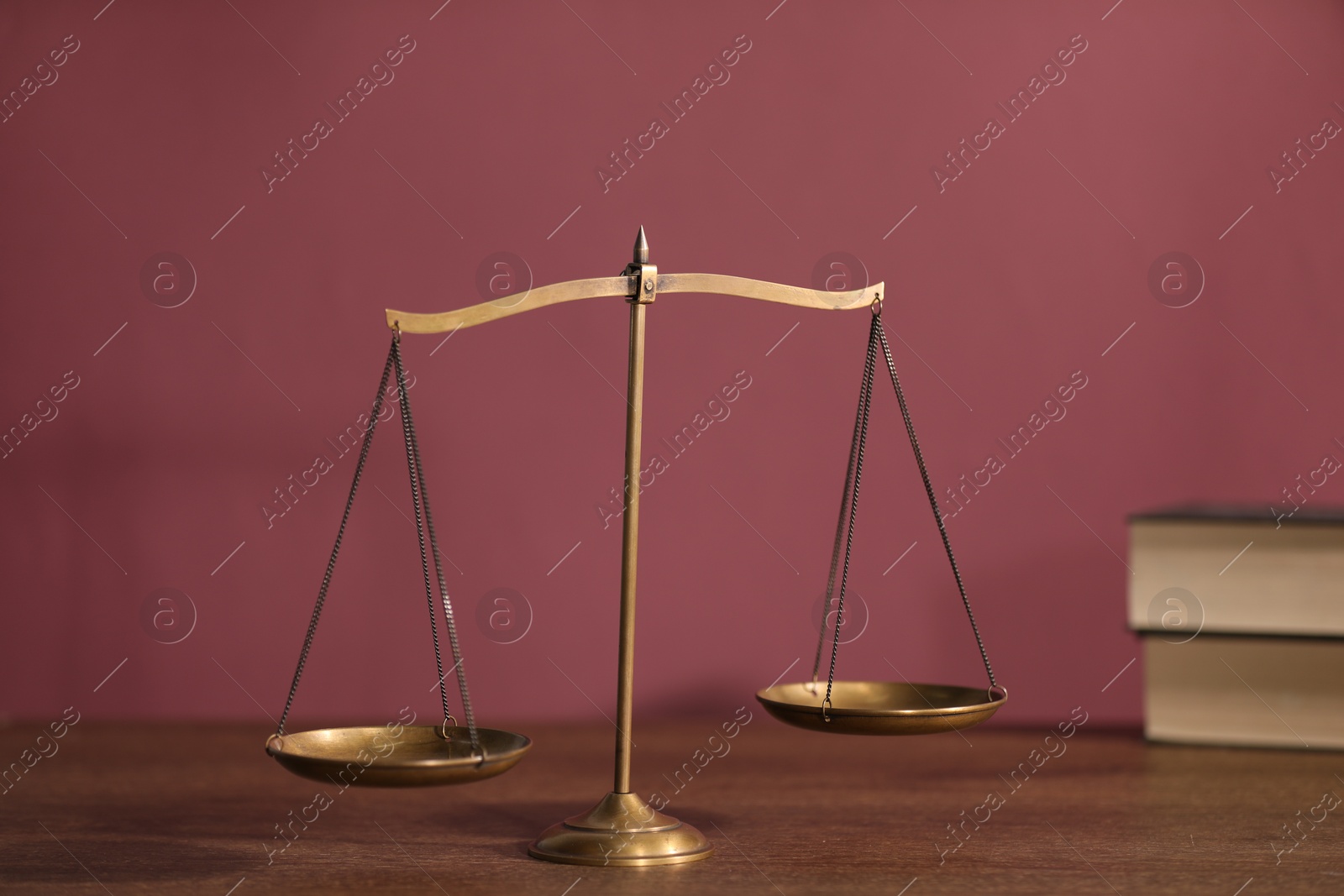 Scales of justice and books on wooden table against color background Photo of Scales of justice and books on wooden table against color background