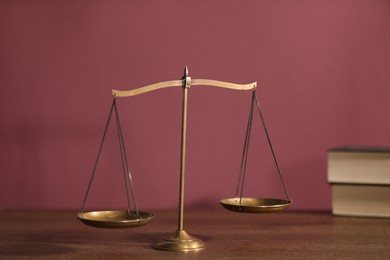 Photo of Scales of justice and books on wooden table against color background