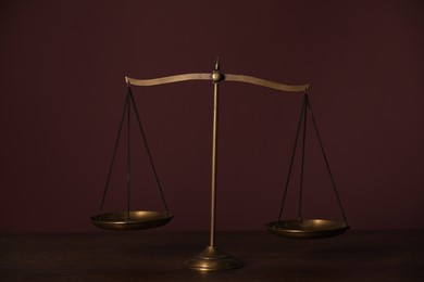 Photo of Scales of justice on wooden table against dark background