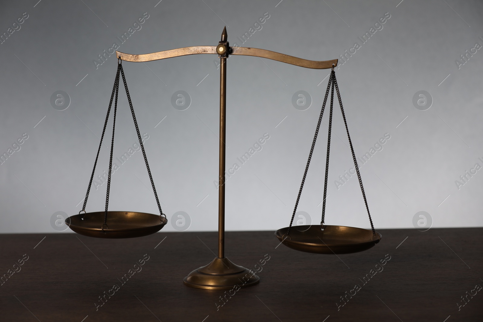 Scales of justice on table against light background Photo of Scales of justice on table against light background
