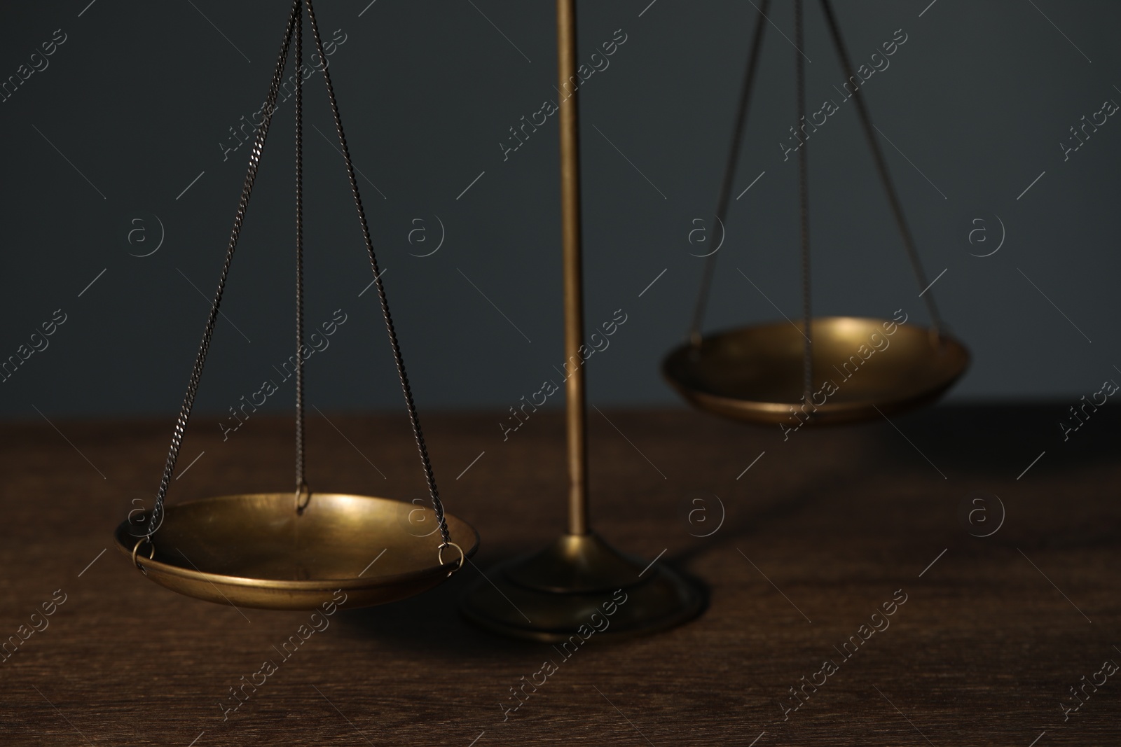 Photo of Scales of justice on wooden table against gray background, closeup
