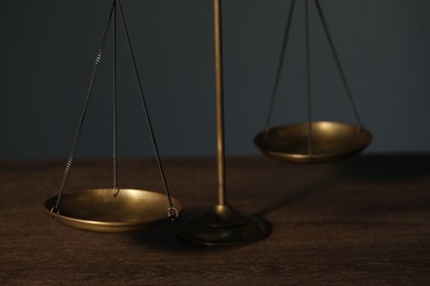 Photo of Scales of justice on wooden table against gray background, closeup