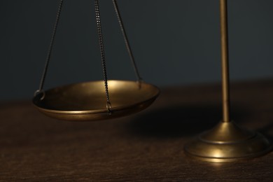 Photo of Scales of justice on wooden table against gray background, closeup