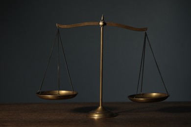 Photo of Scales of justice on wooden table against gray background
