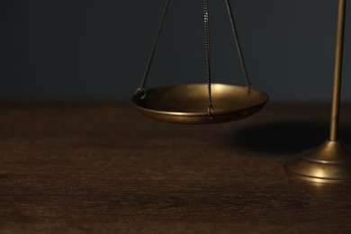 Photo of Scales of justice on wooden table against gray background, closeup. Space for text
