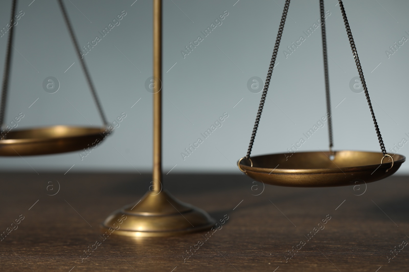 Photo of Scales of justice on wooden table against light background, closeup