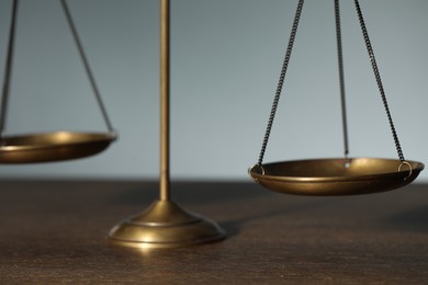 Photo of Scales of justice on wooden table against light background, closeup