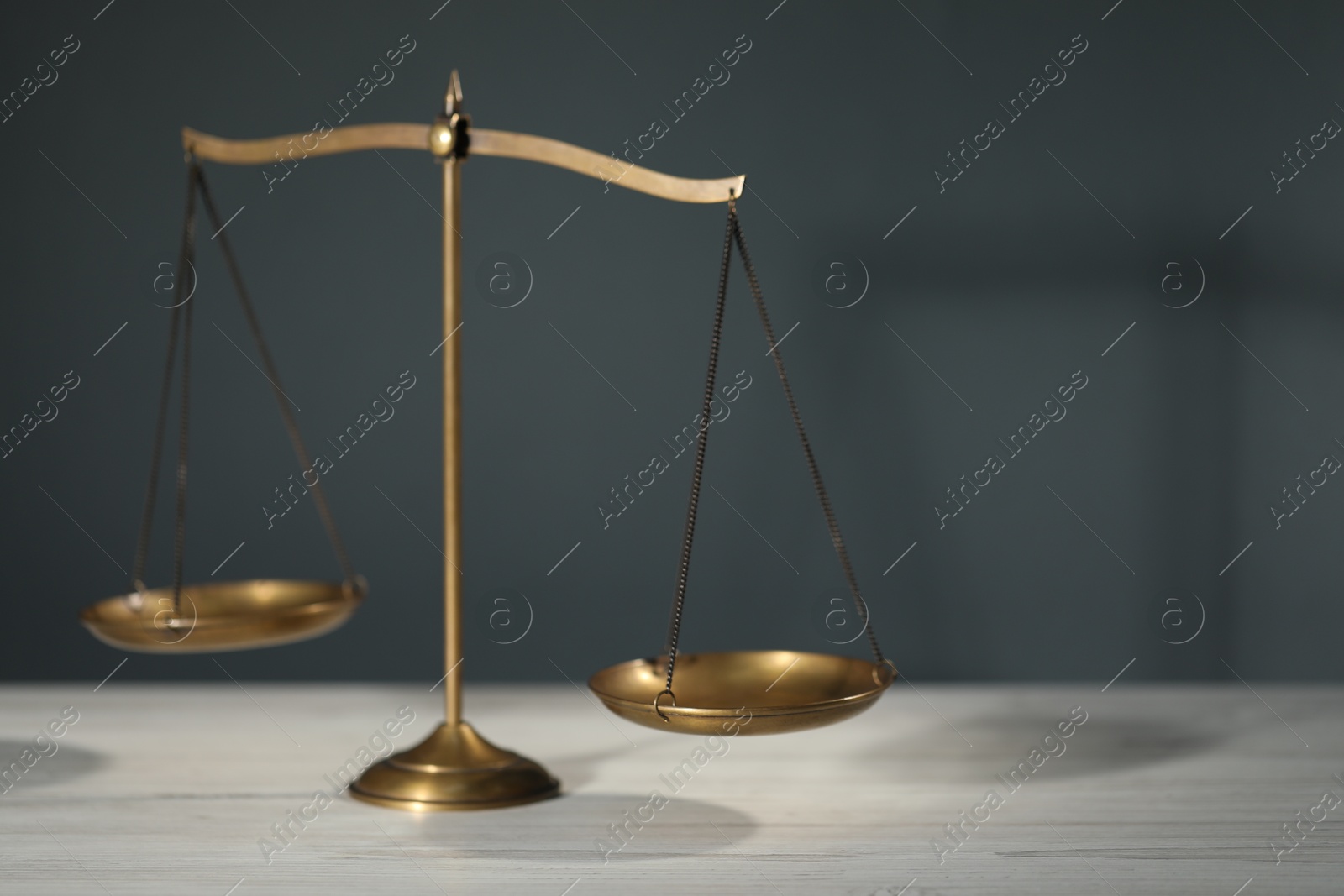 Scales of justice on light wooden table against gray background Photo of Scales of justice on light wooden table against gray background
