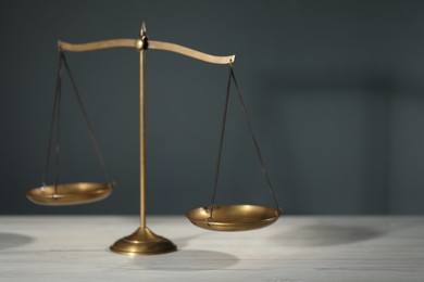 Photo of Scales of justice on light wooden table against gray background