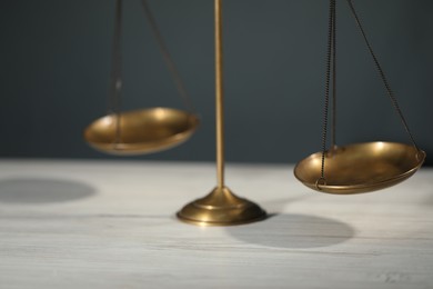 Photo of Scales of justice on light wooden table against gray background, closeup