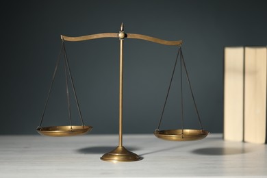 Photo of Scales of justice and books on light wooden table against gray background, selective focus