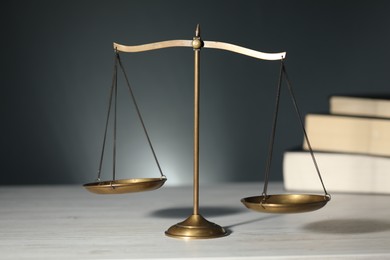 Photo of Scales of justice and books on light wooden table against gray background, selective focus
