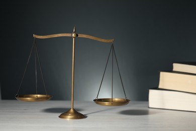 Photo of Scales of justice and books on light wooden table against gray background